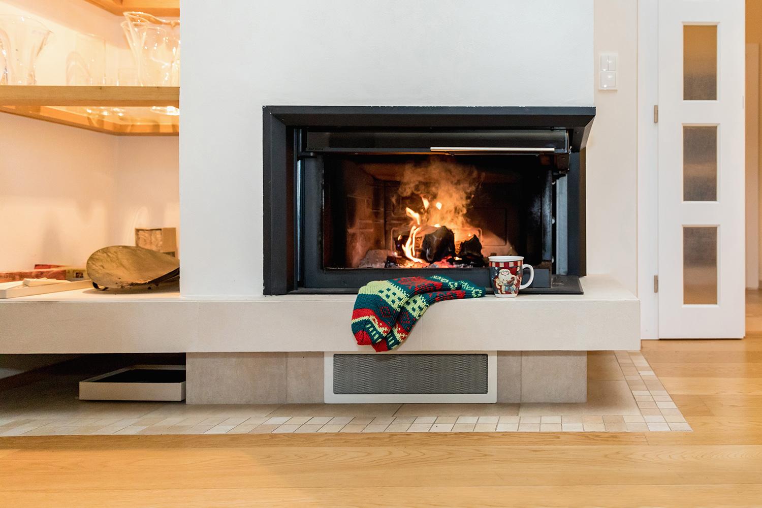 Woollen socks by the Christmas fireplace. Wool socks at a modern Christmas fireplace. Close up on feet. Winter and Christmas holidays concept.